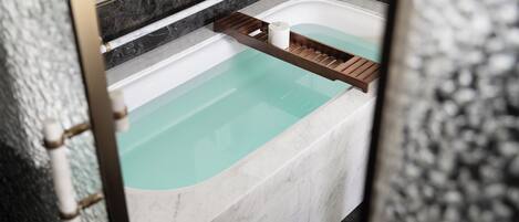 Una bañera con una bandeja de madera y una botella blanca.