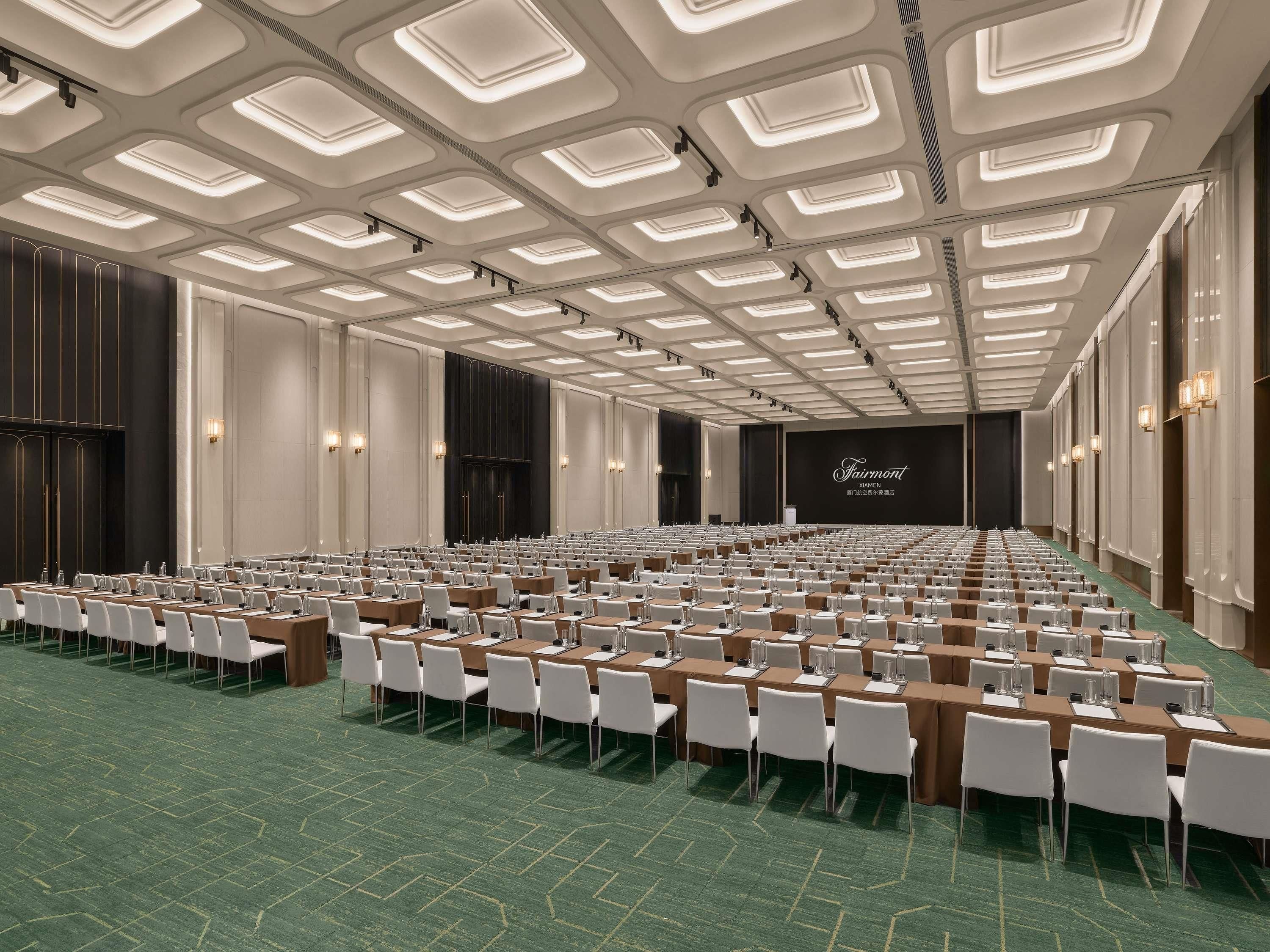 Ein Konferenzraum mit Tischen und Stühlen, einer Bühne mit einem Bildschirm und einem modernen Deckenstil.