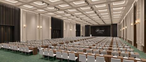 Ein Konferenzraum mit Tischen und Stühlen, einer Bühne mit einem Bildschirm und einem modernen Deckenstil.