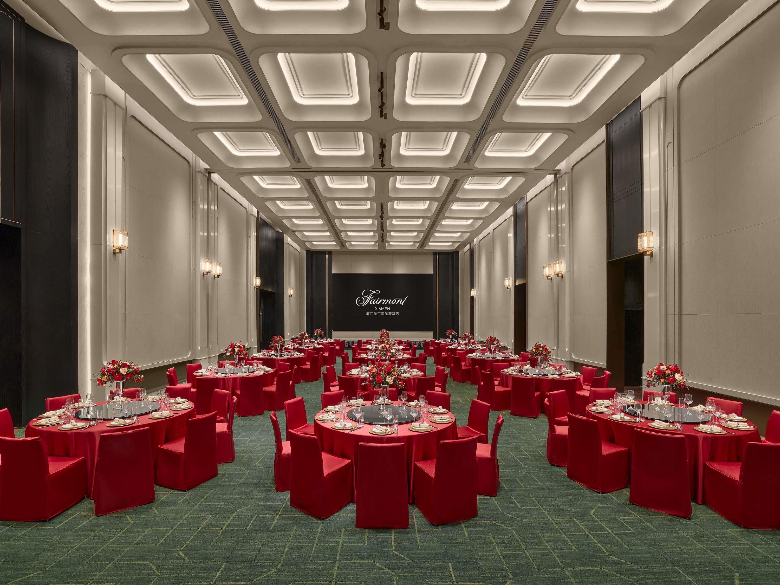 A conference room with multiple tables set for dining, red chairs, and a large screen in the background.