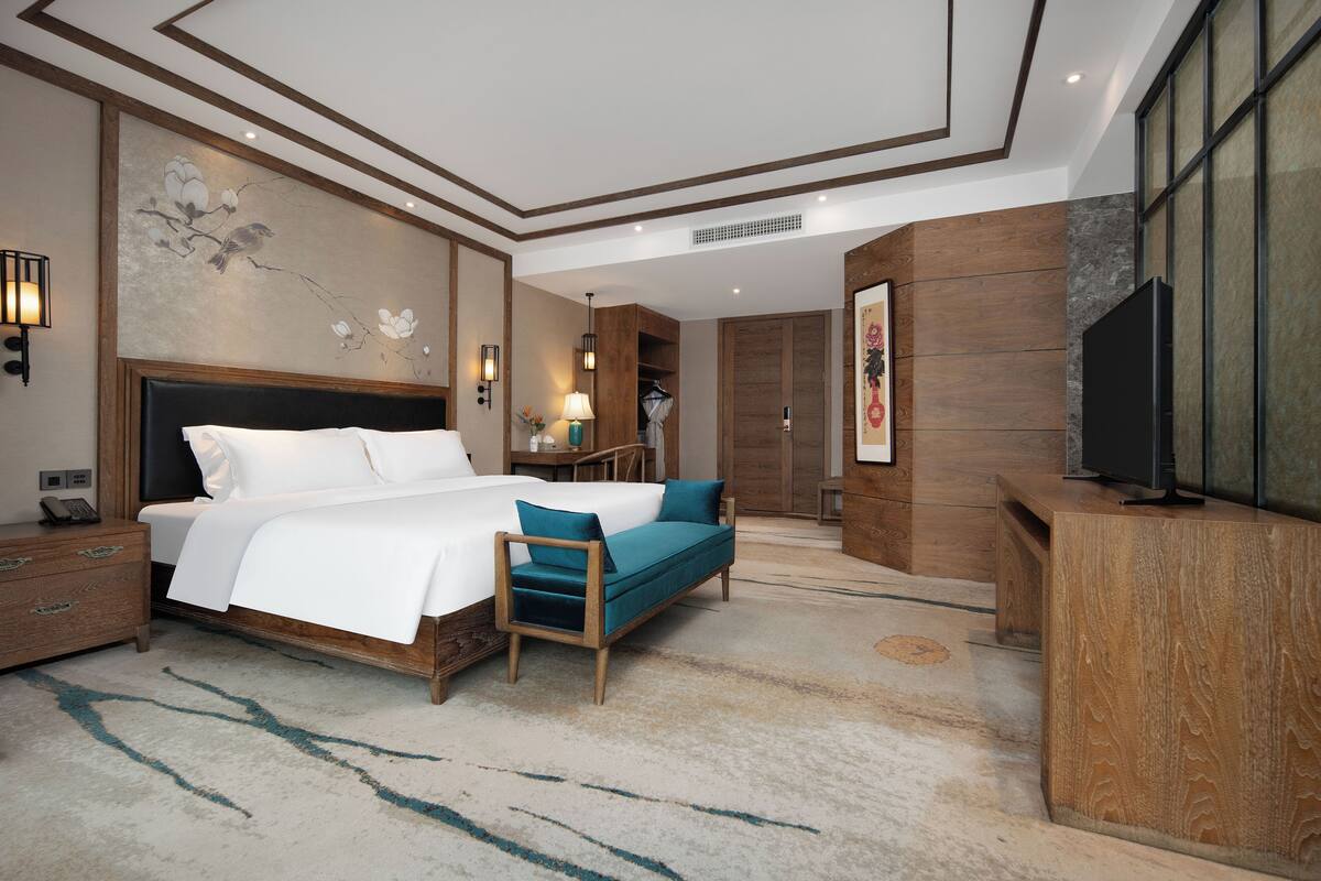 A modern hotel room with a large bed, a desk, a television, and a seating area.