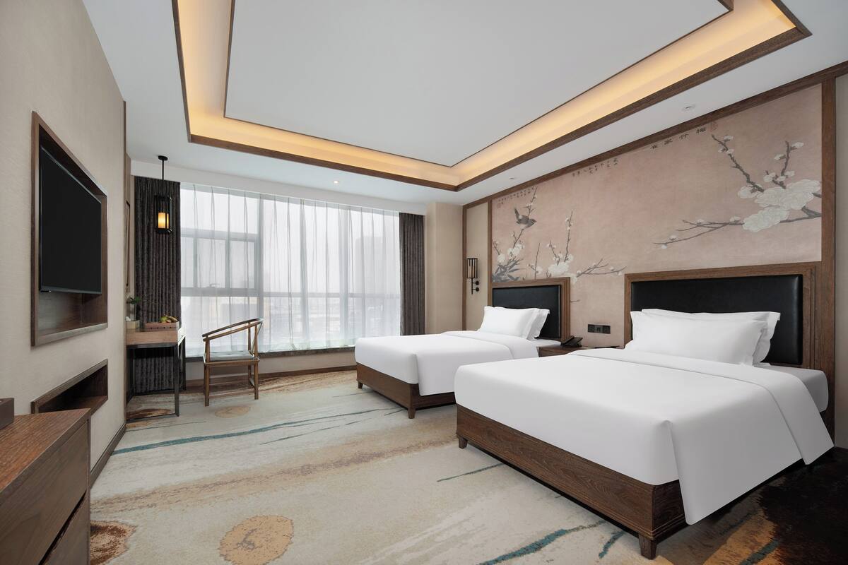 A modern hotel room with two beds, a desk, and a TV.