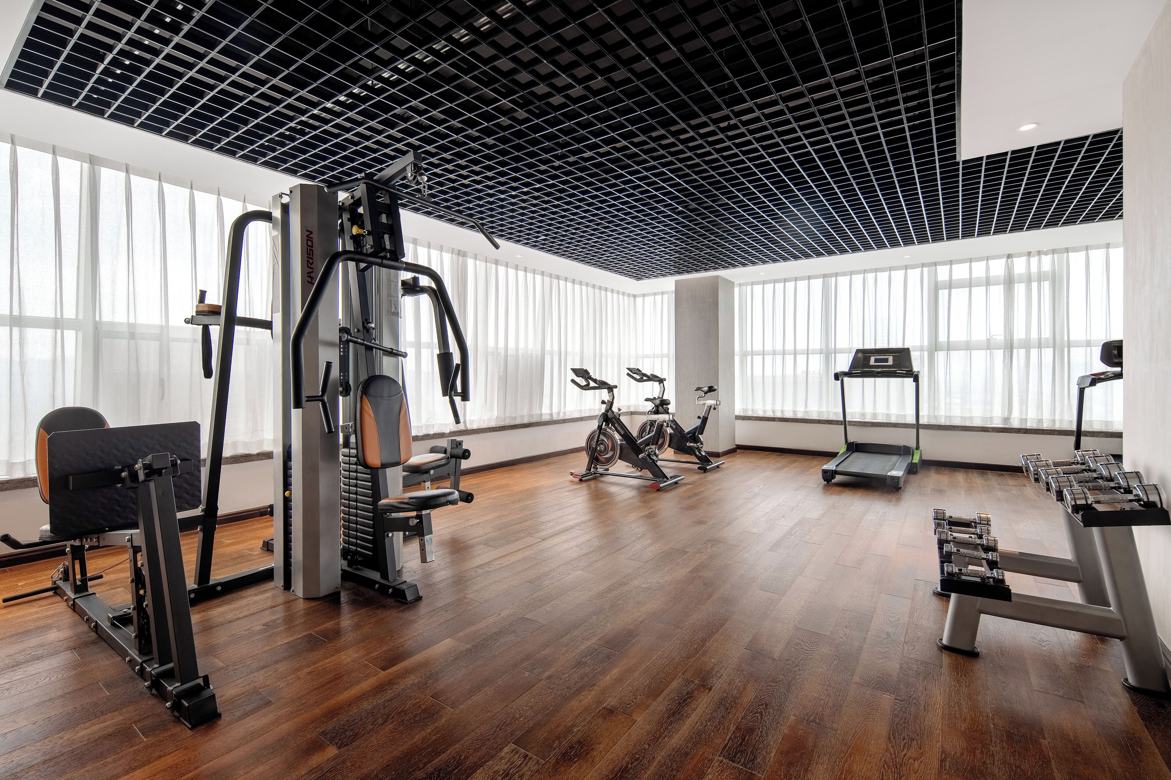 A gym with various exercise equipment, large windows, and a wooden floor.