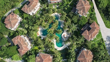 A resort with multiple buildings, a central swimming pool, and surrounding palm trees.