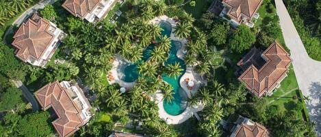 Ein Resort mit mehreren Gebäuden, einem zentralen Pool und umliegenden Palmen.
