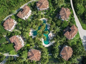 Ein Resort mit mehreren Gebäuden, einem zentralen Pool und umliegenden Palmen.