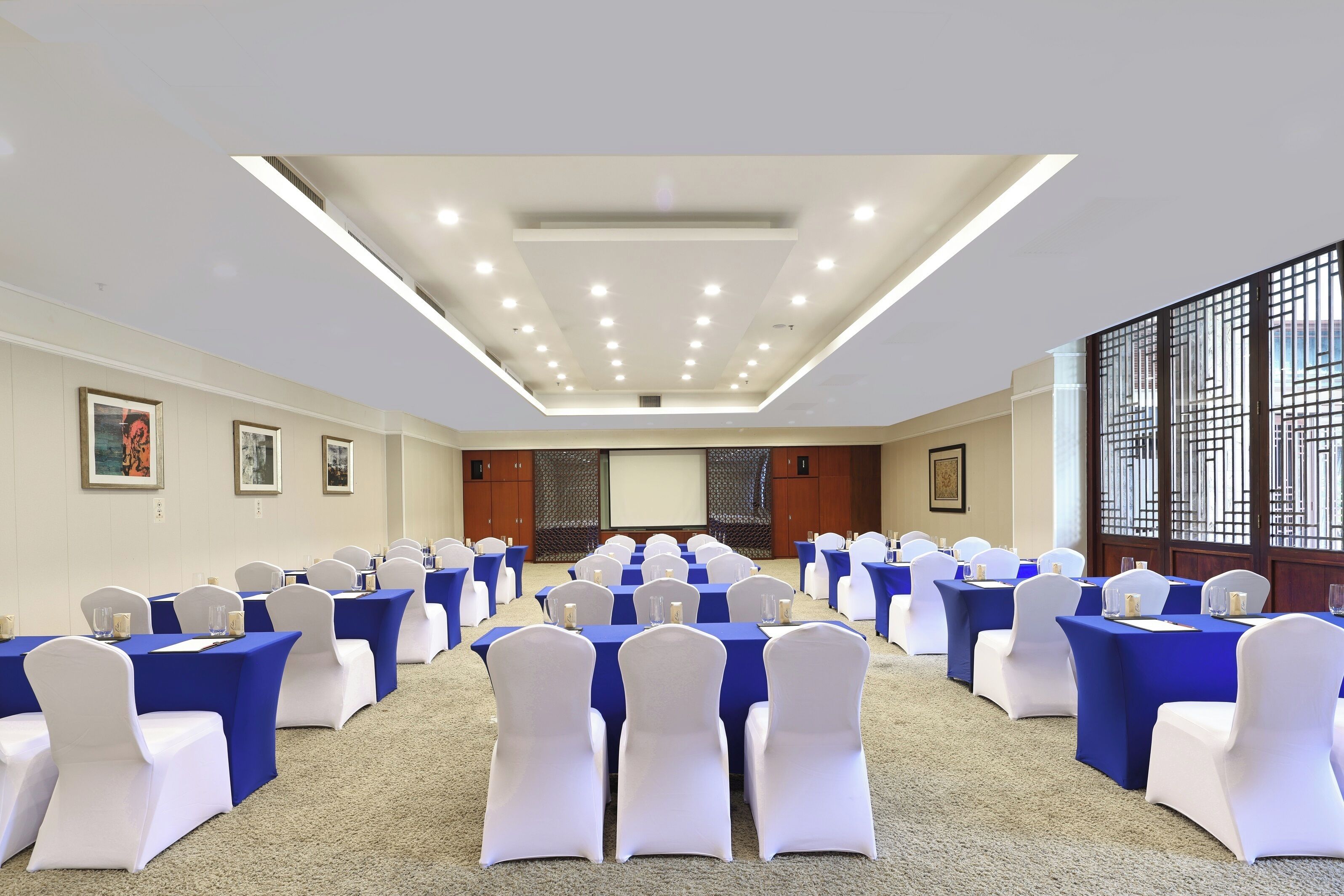 A conference room with rows of tables and chairs, a projector screen, and a large window with a view.