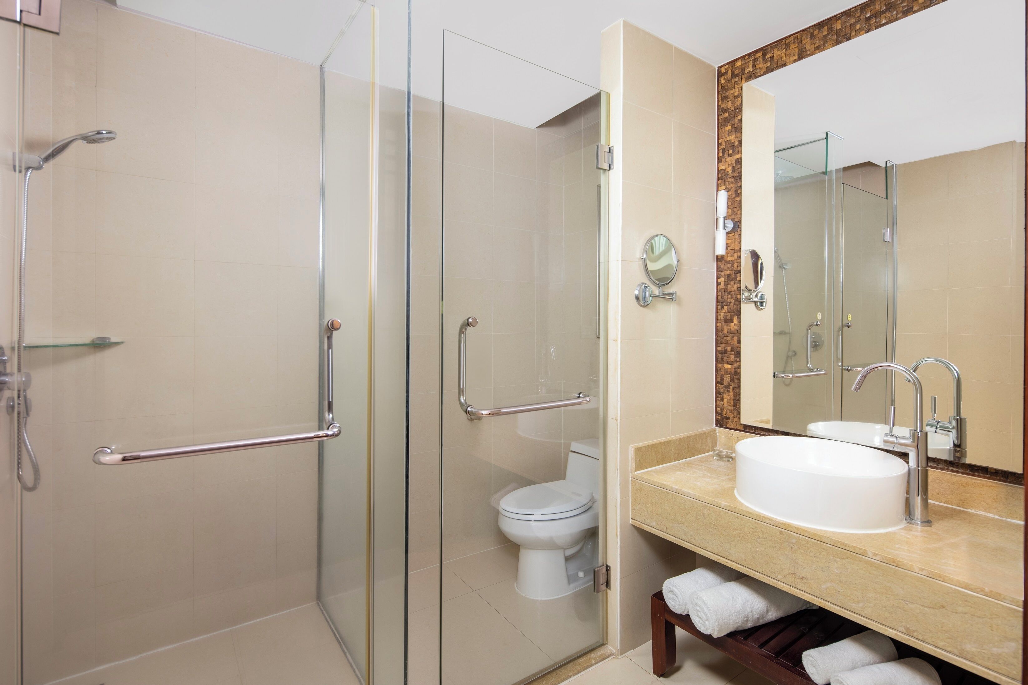 Een moderne badkamer met een douchecabine van glas, een wit toilet en een wastafel met een grote spiegel erboven.