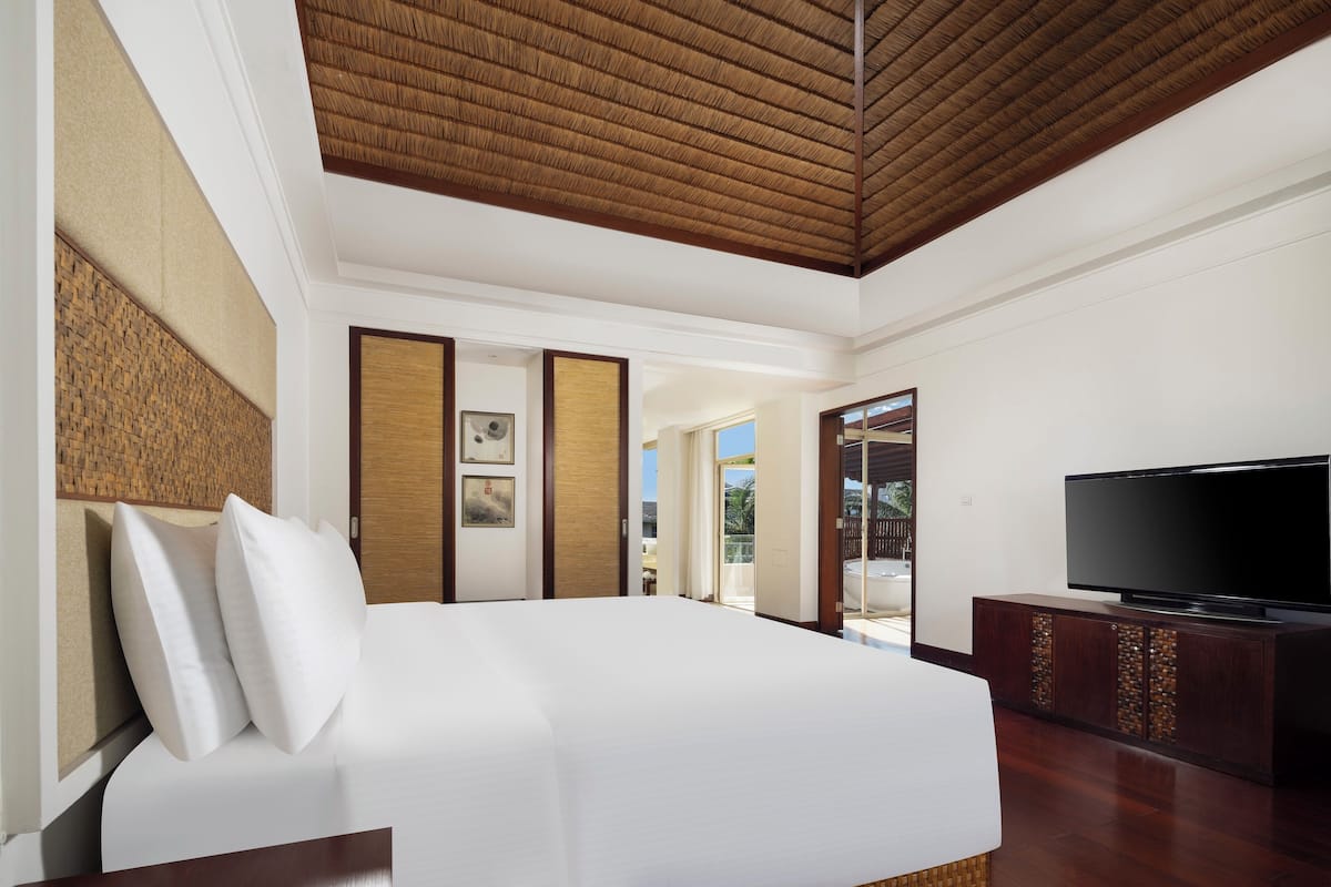 A modern hotel room with a large bed, a flat-screen TV, and a wooden ceiling.