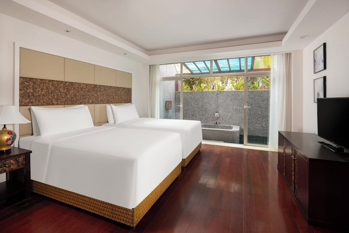 A hotel room with a large bed, a TV, a bathroom with a shower, and a balcony with a view of greenery.