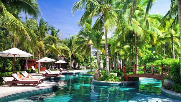 A pool area with lounge chairs and umbrellas, surrounded by palm trees. - Grand Mercure Sanya Yalong Bay  (Sanya)