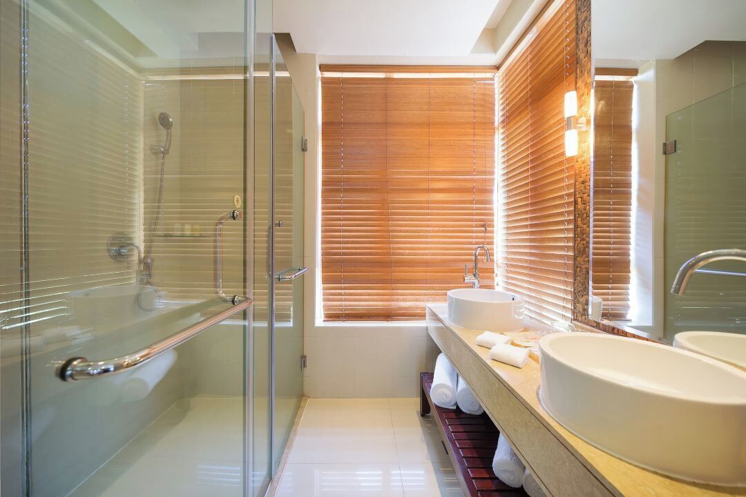 A modern bathroom with a glass shower enclosure, a wooden vanity with two sinks, and a large mirror.