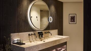 A modern bathroom with a large vanity, a round mirror with a light, and a framed picture on the wall.