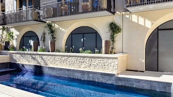 A modern building with a swimming pool, arched windows, and outdoor seating.