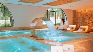 A spa pool with a waterfall feature, lounge chairs, and a stone wall.
