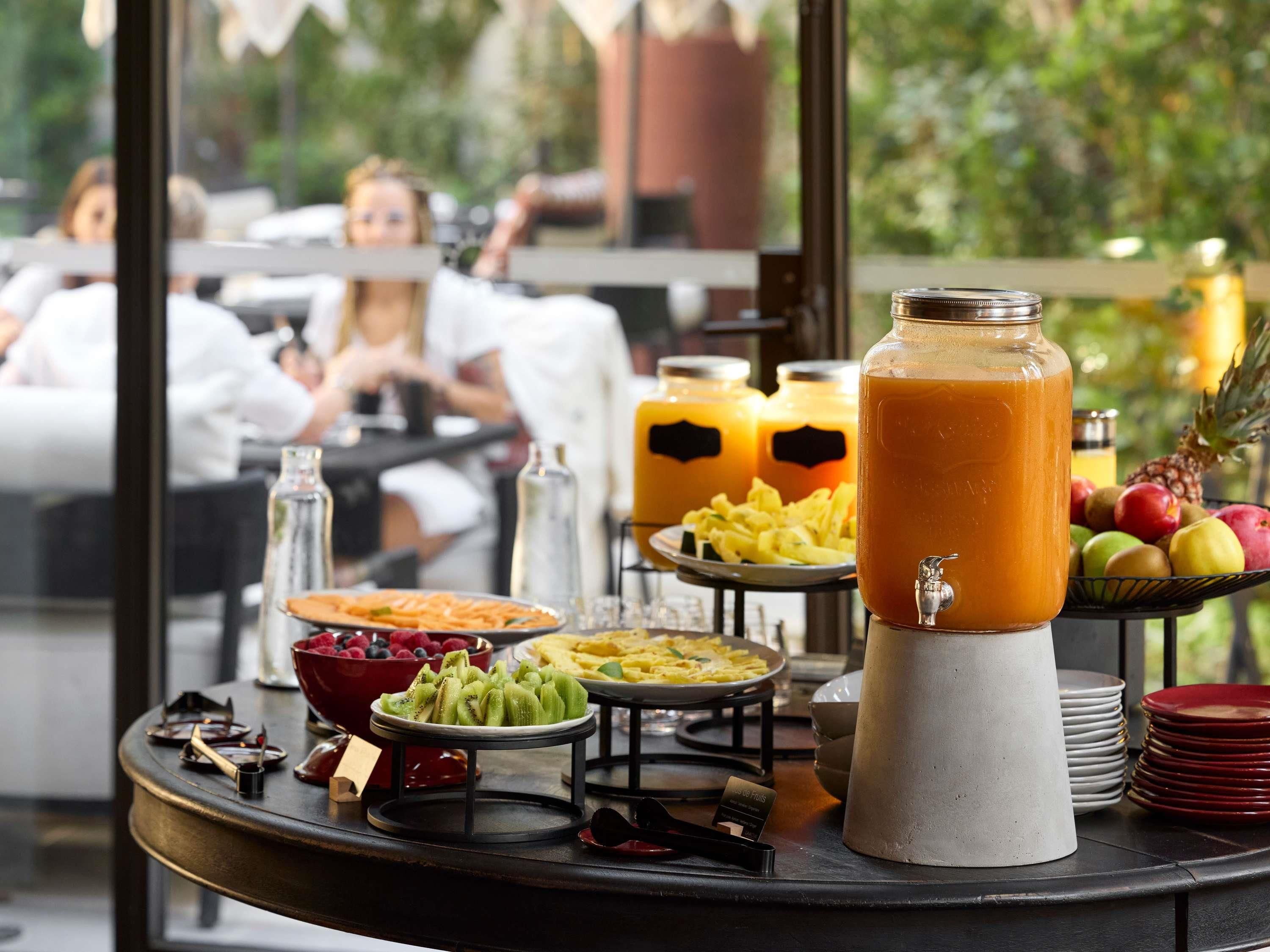 Un bufé de desayuno con una variedad de frutas, un dispensador grande de jugo y vistas al exterior.