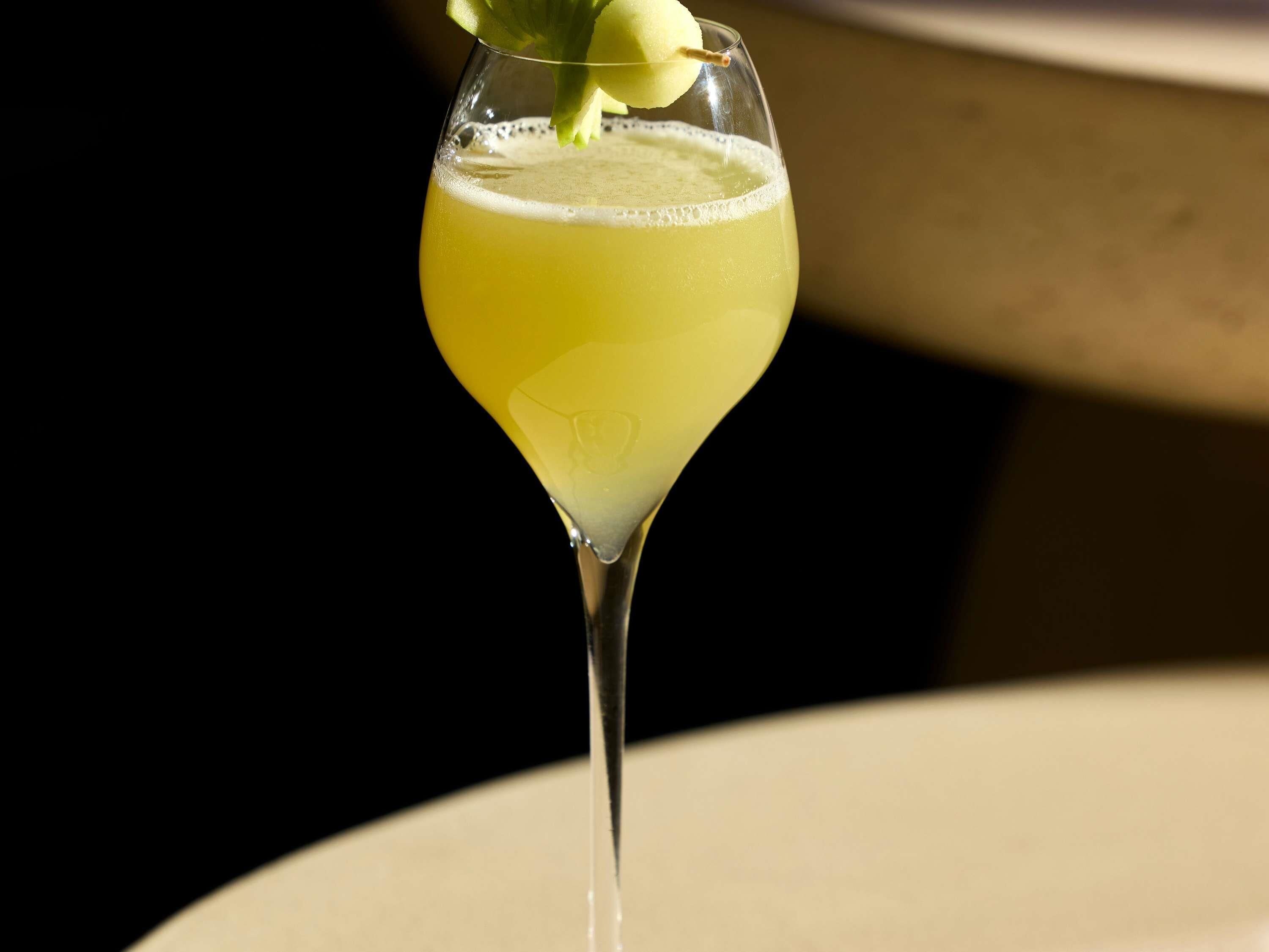 A cocktail in a martini glass with a lemon garnish on a table.