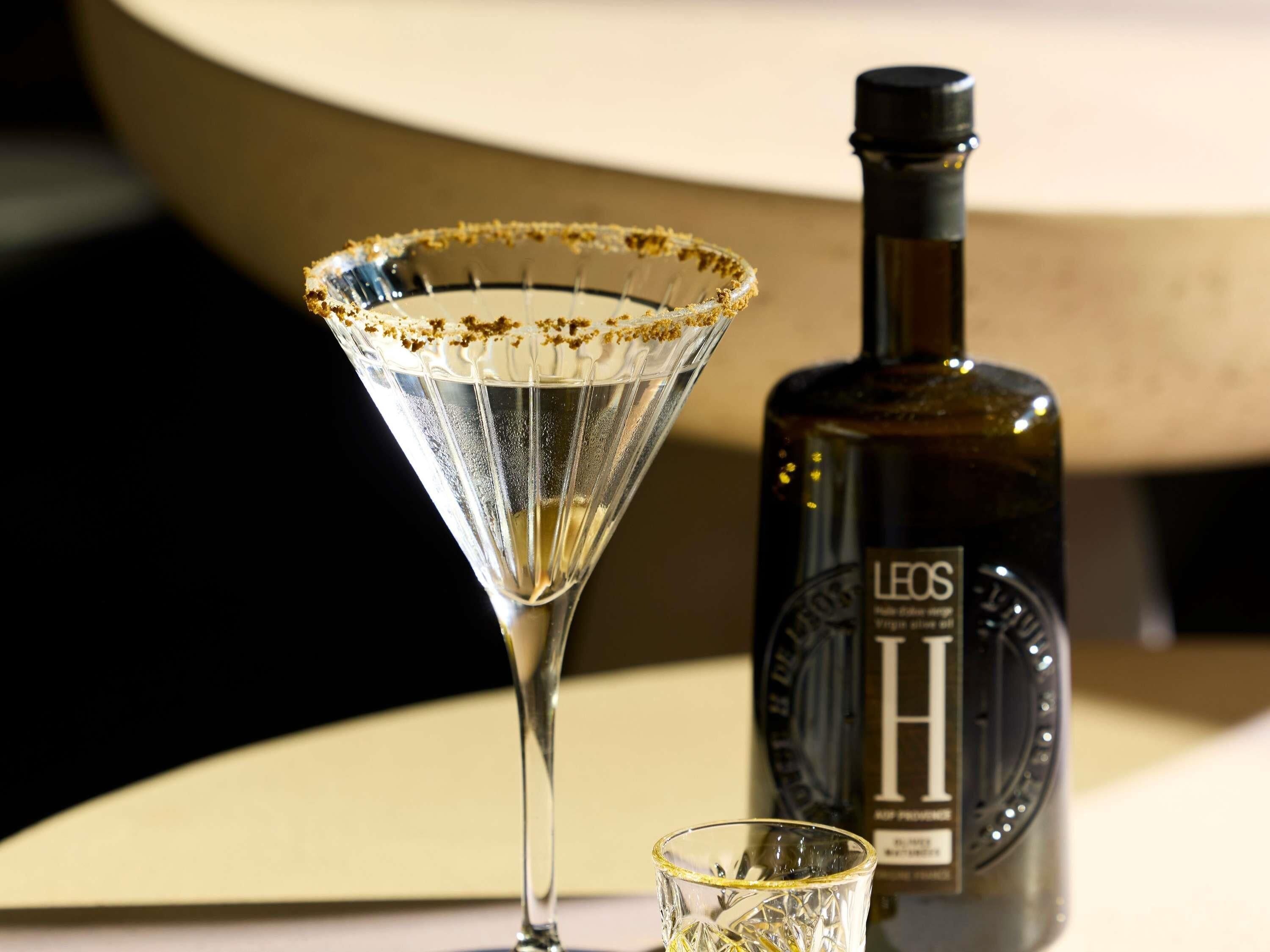 A martini glass with a salted rim, a bottle of alcohol, and a small glass.