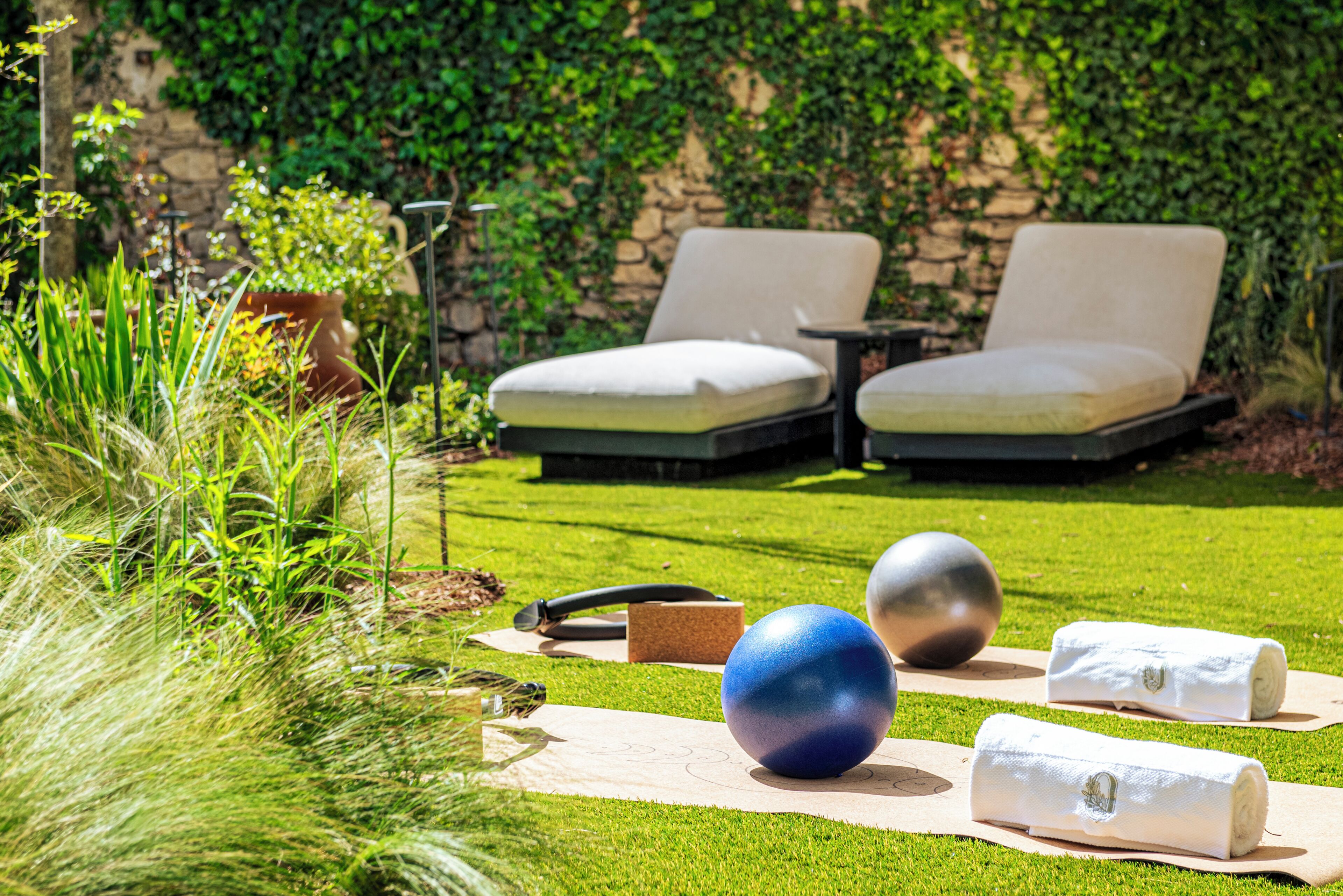 A grassy outdoor area with two lounge chairs, exercise equipment, and a stone wall with greenery.