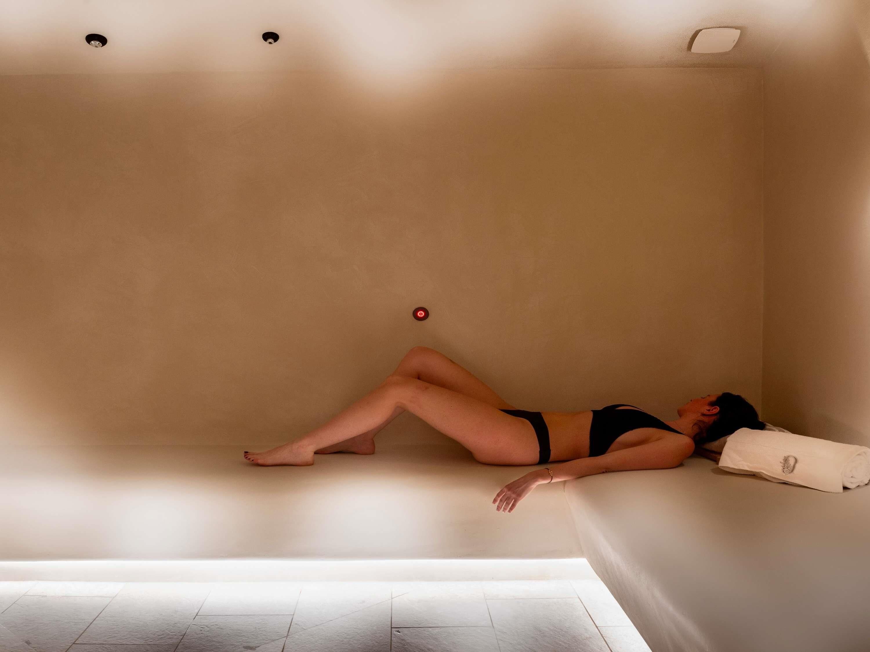 A person lying in a bathtub with a towel and a remote control on the wall.