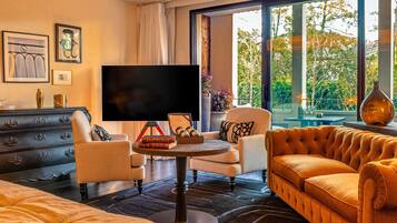 Une chambre d’hôtel moderne dotée d’une grande fenêtre, d’un téléviseur à écran plat, d’un canapé, d’un fauteuil, d’une petite table et d’une commode.