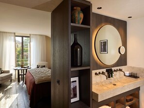 Ein Hotelzimmer mit Bett, Schreibtisch, Stuhl, einem großen Spiegel und einem Badezimmer mit Waschbecken und Dusche.
