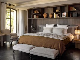 Un dormitorio con una cama grande, una mesita de noche, una silla, una estantería y una ventana.