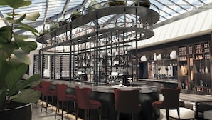 En moderne bar med et buet loft og en central spiraltrappe. Der er flere hylder med flasker og glas, samt en bardisk med skrammel.