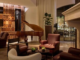 A grand piano in a spacious lounge area with leather armchairs and a large potted plant.
