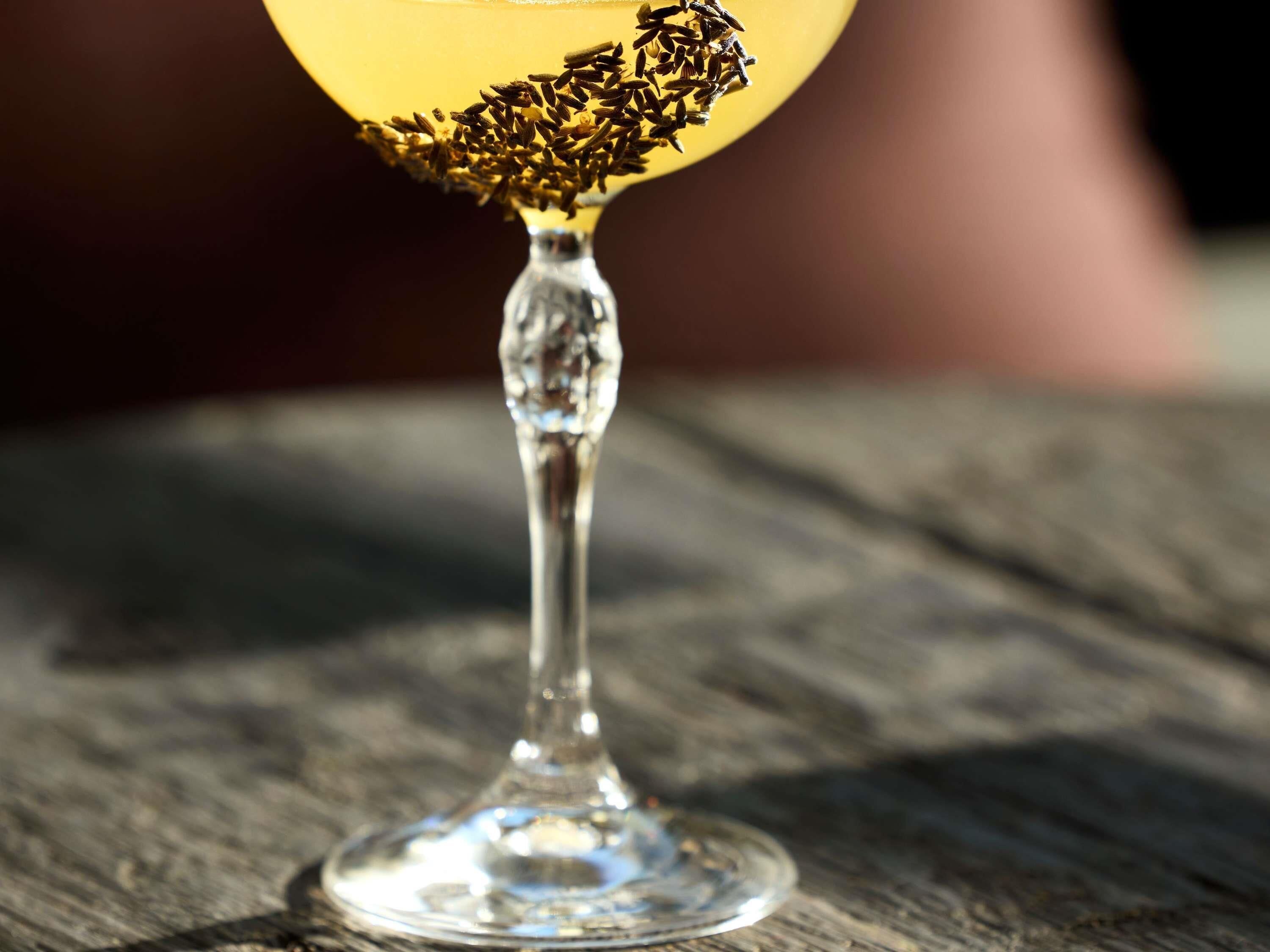 A clear glass with a dark liquid and a garnish of black seeds on a wooden surface.