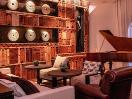 Una habitación con un piano de cola, un papel tapiz decorativo y una zona de estar con una mesa redonda y sillas.
