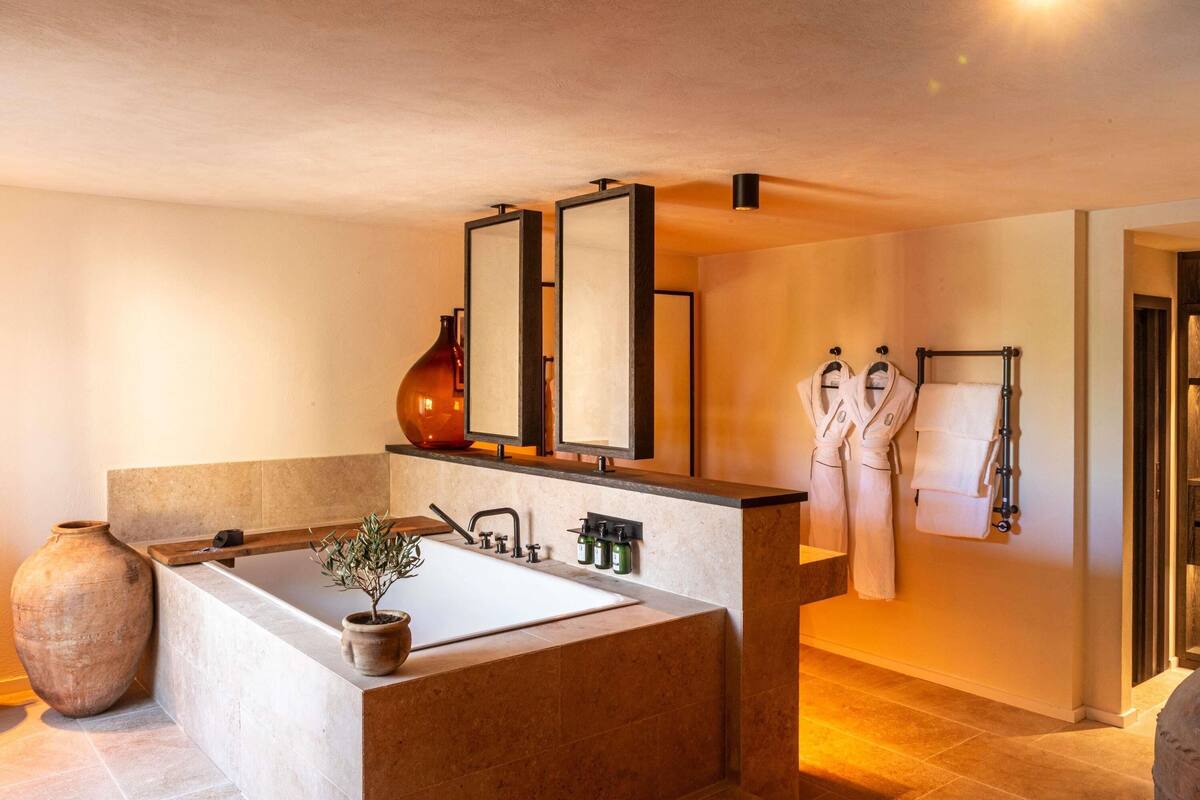 A modern bathroom with a large bathtub, a mirror, a vase, and towels on a rack.