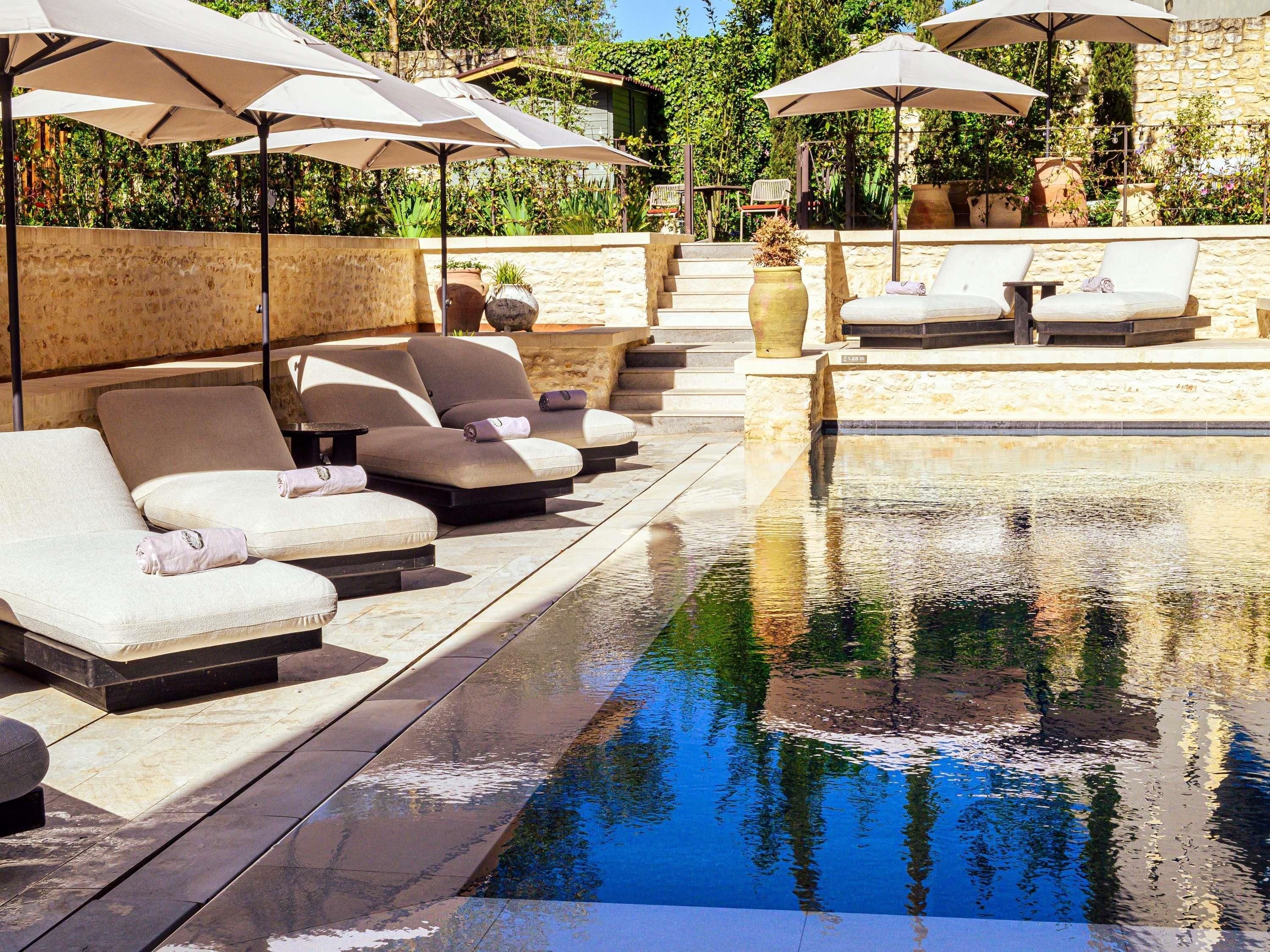 A poolside area with lounge chairs and umbrellas, surrounded by stone walls and greenery.