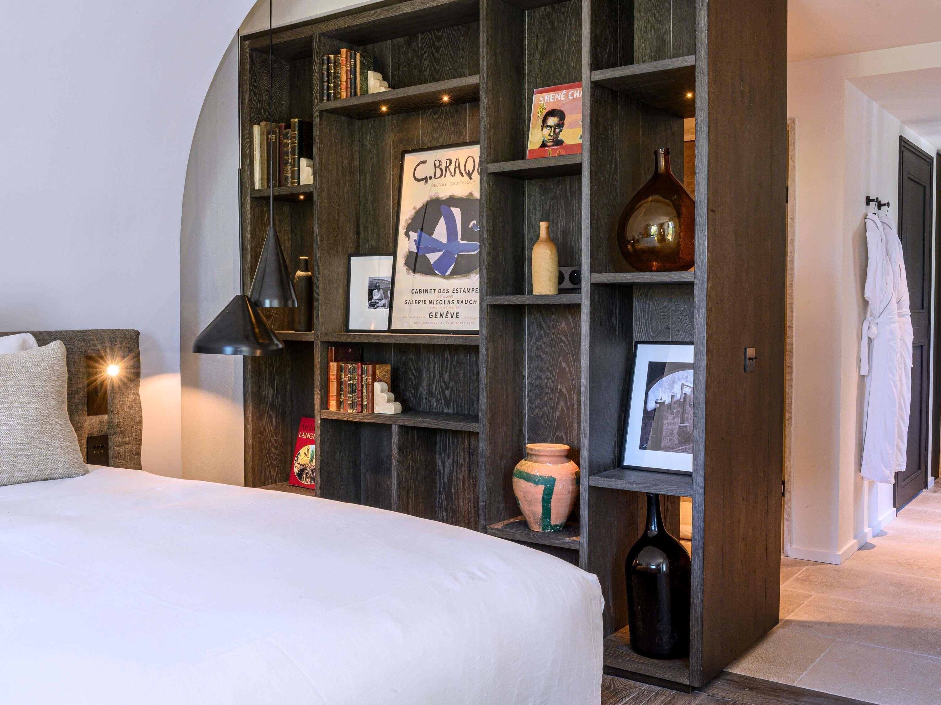 A bedroom with a bed, a bookshelf, a lamp, and a robe hanging on the door.