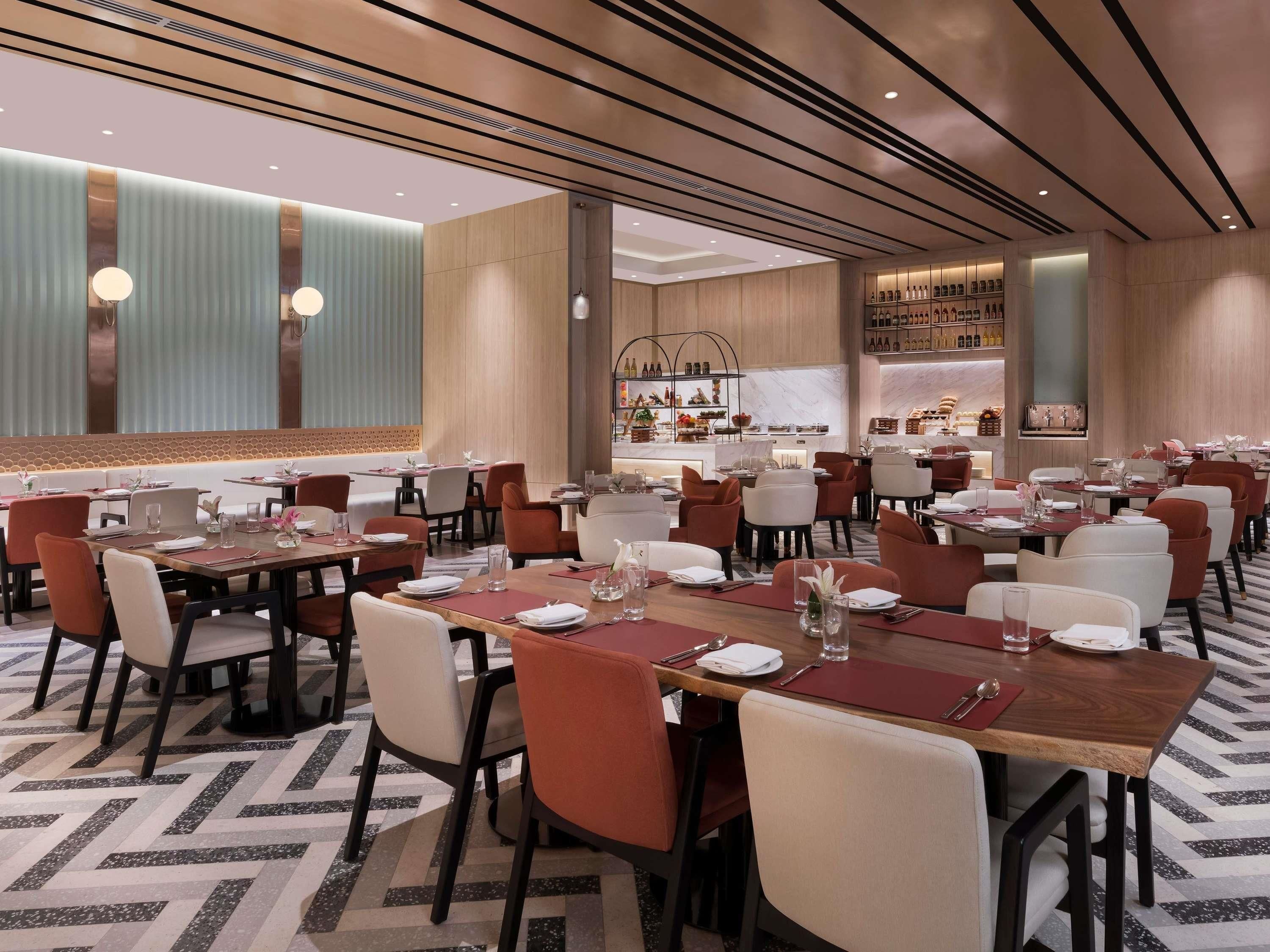 A modern restaurant with multiple dining tables and chairs, a kitchen area in the background, and a patterned floor.