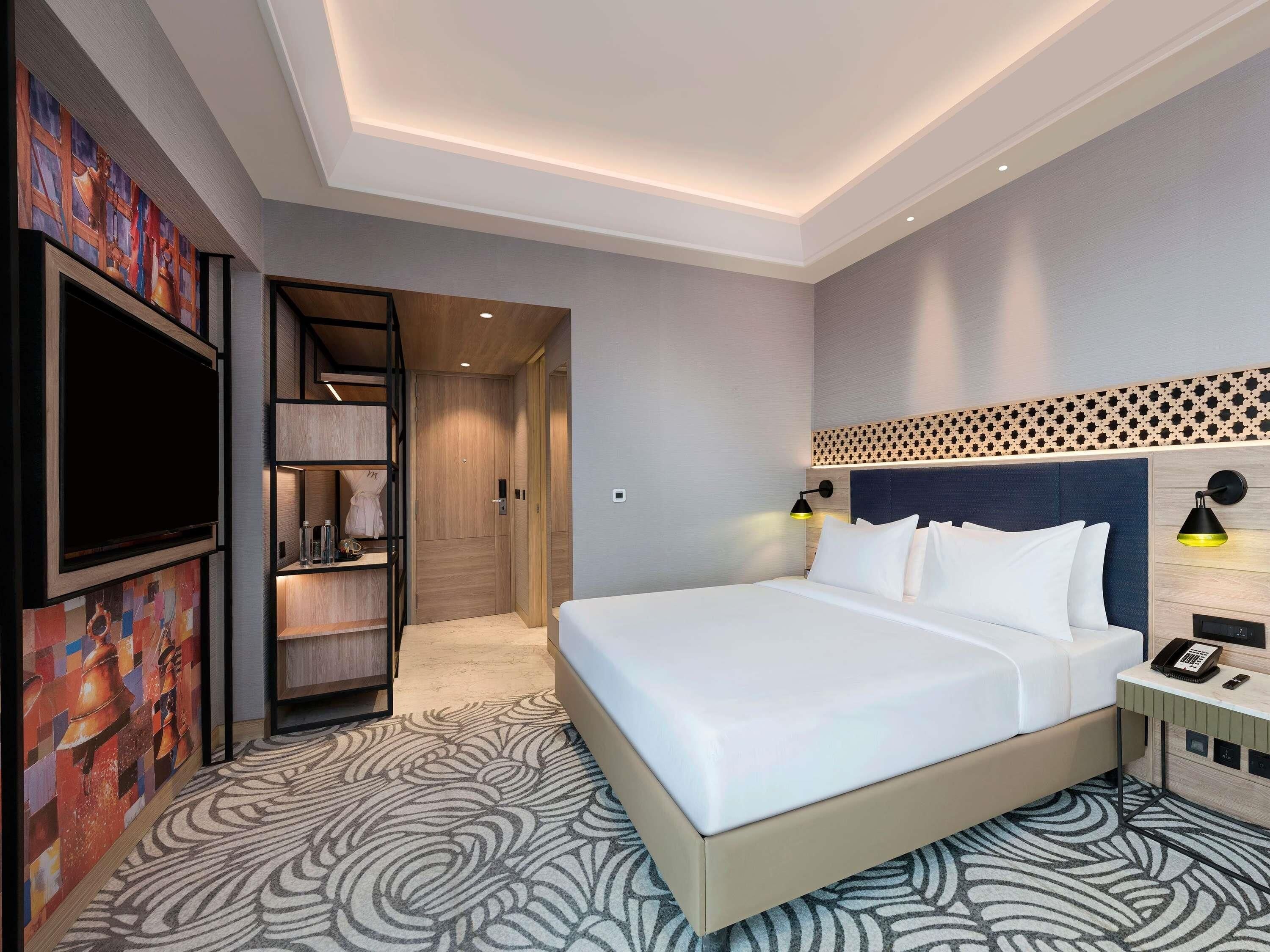 Een hotelkamer met een bed, een televisie, een bureau met telefoon en een wandlamp.