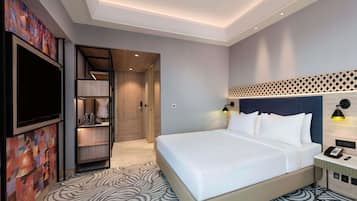 A hotel room with a bed, a TV, a desk with a phone, and a wall-mounted lamp.