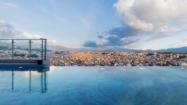 Piscina infinita no terraço com guarda-corpo de vidro e vista para a paisagem urbana.