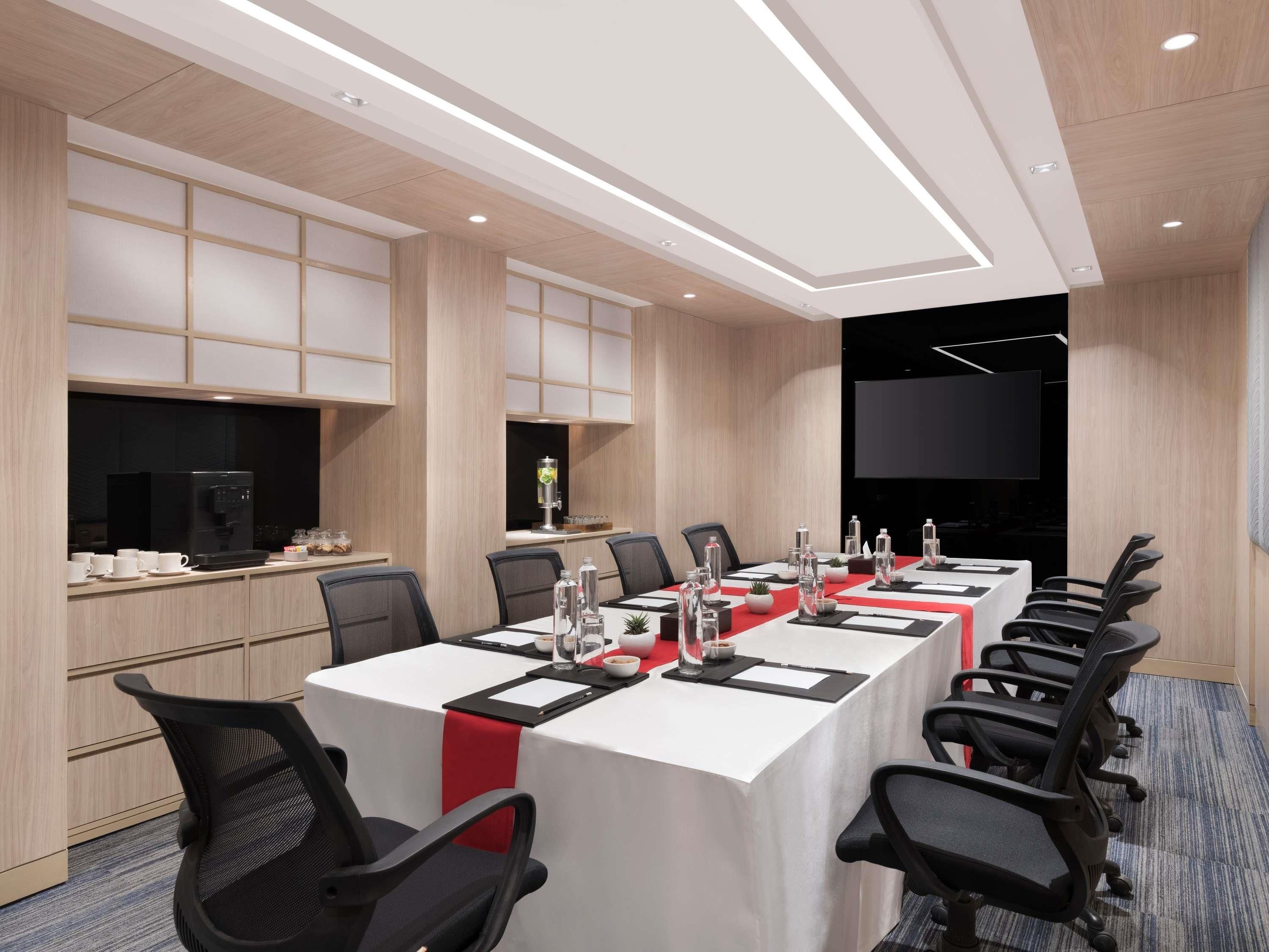 A conference room with a long table, chairs, a coffee machine, and a TV screen.