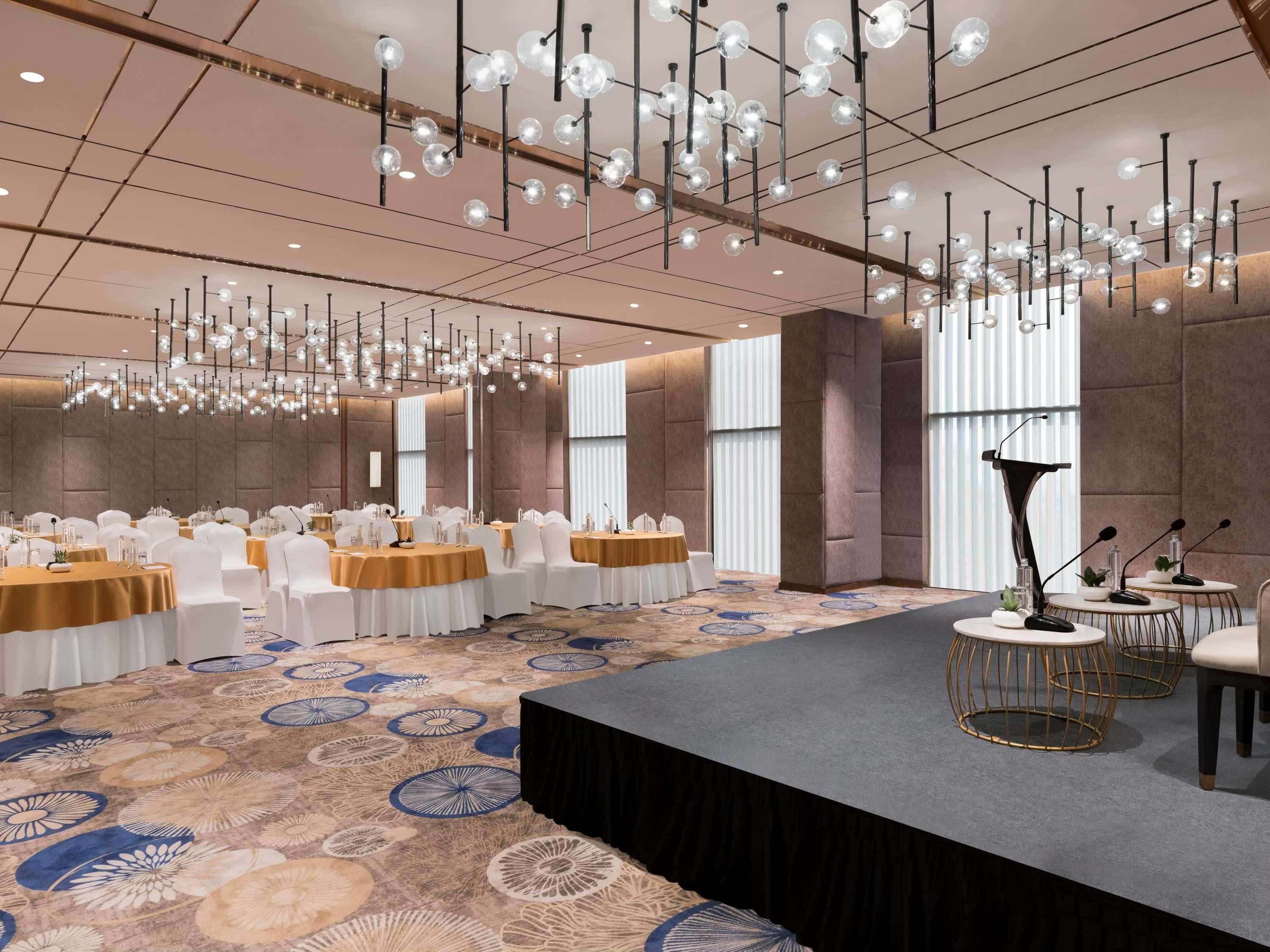 Un salón de conferencias con mesas redondas, sillas blancas y un escenario con un atril.