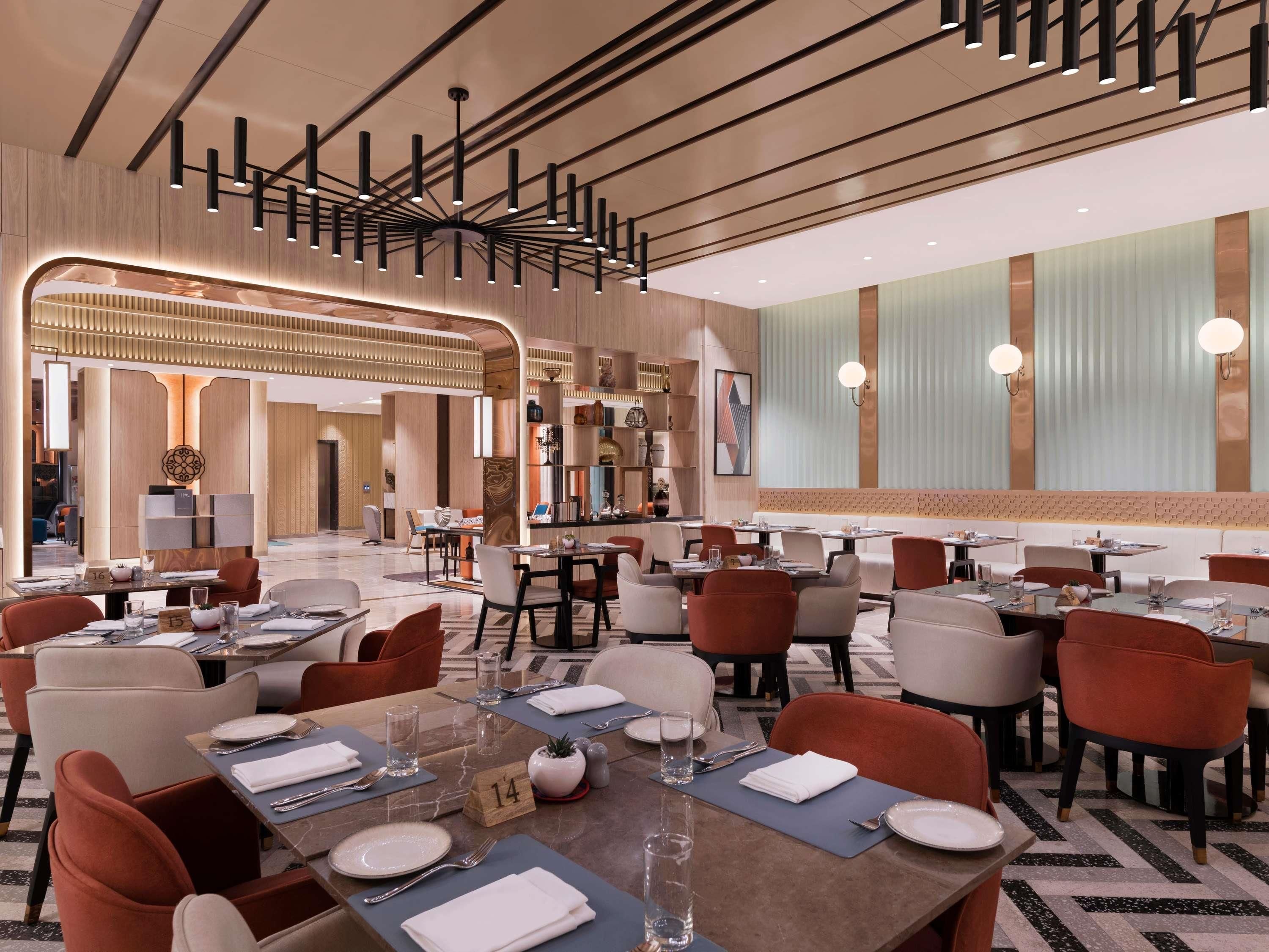 A modern restaurant with multiple dining tables, chairs, and a central light fixture.