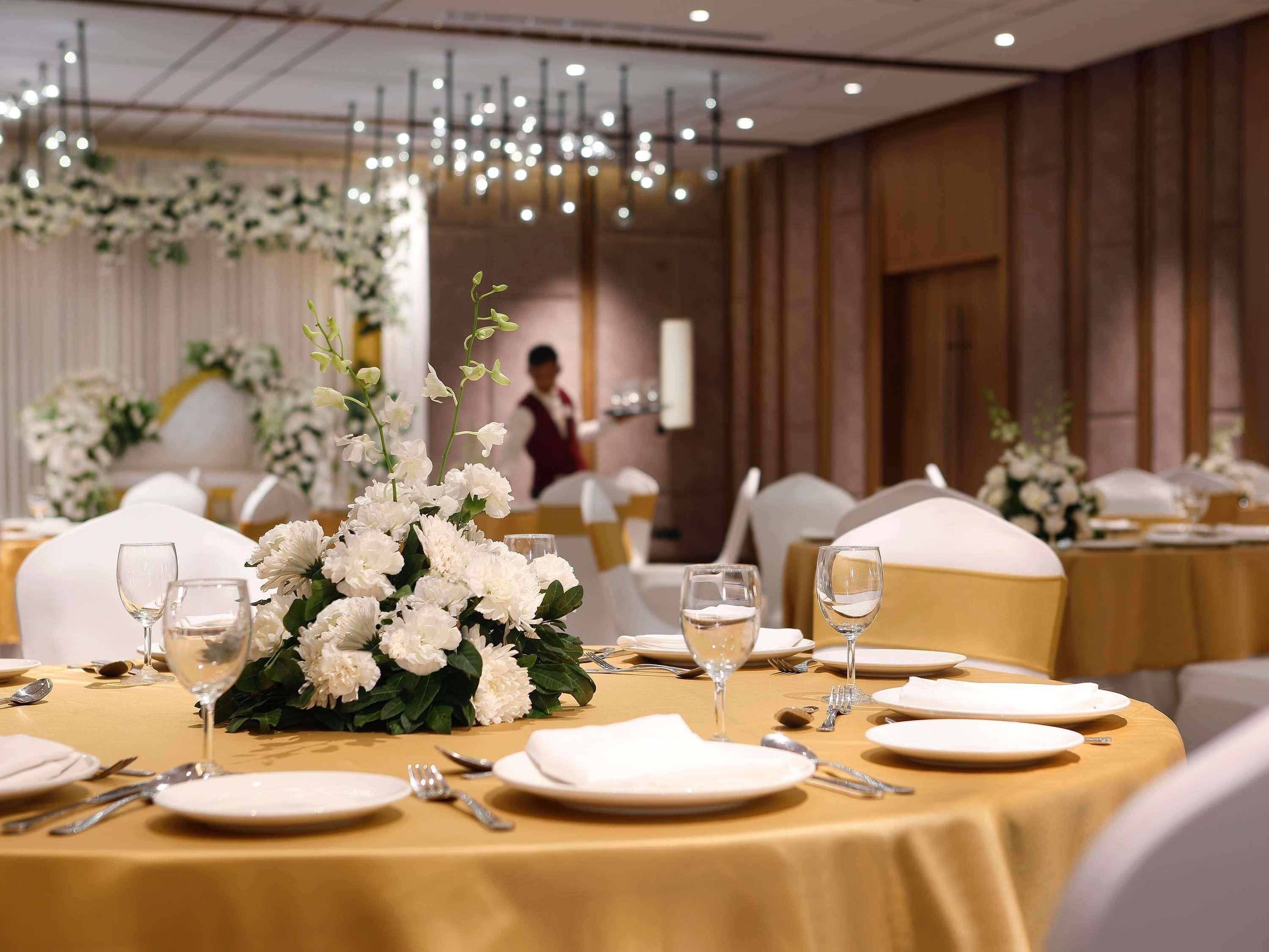 A banquet hall with round tables set for dining, featuring white floral centerpieces and gold tablecloths.