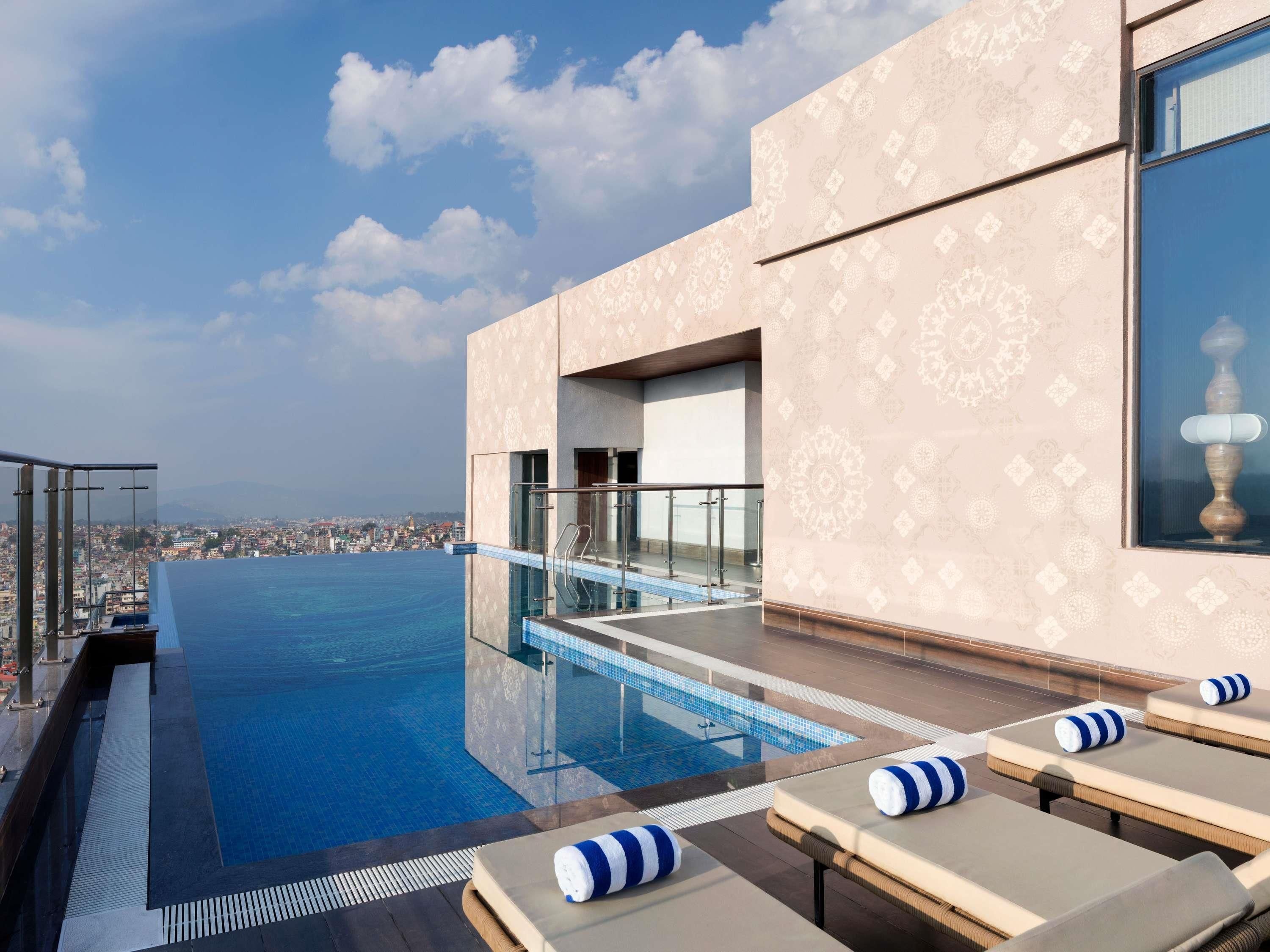 A rooftop infinity pool with lounge chairs and a city view.