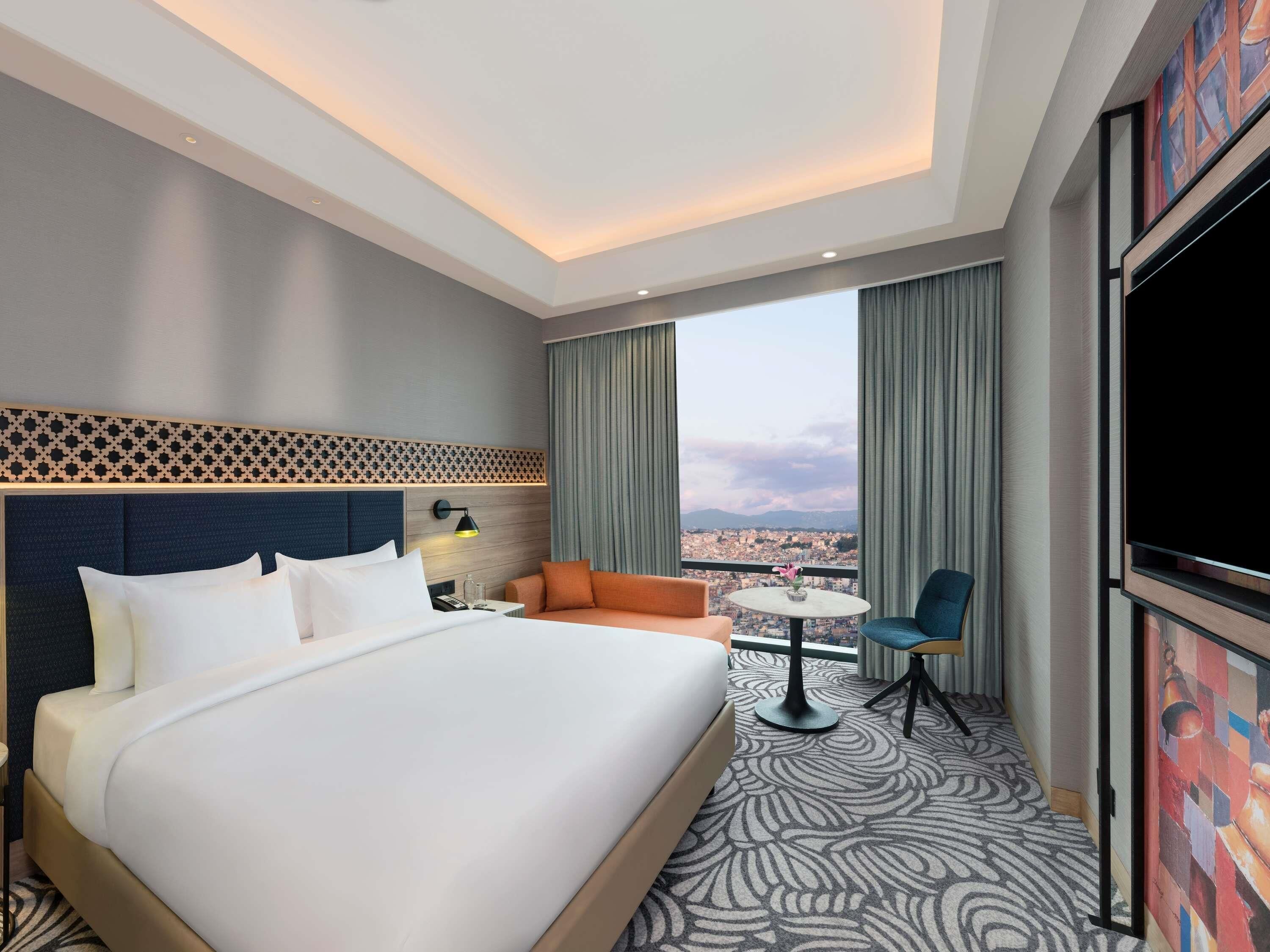 A hotel room with a large bed, a sofa, a small table, and a TV.