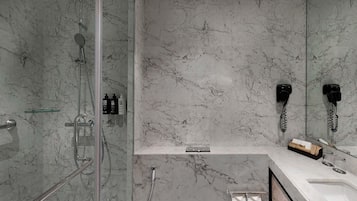 A modern bathroom with a glass-enclosed shower, a marble-tiled wall, a white sink, and a mirror with a telephone.
