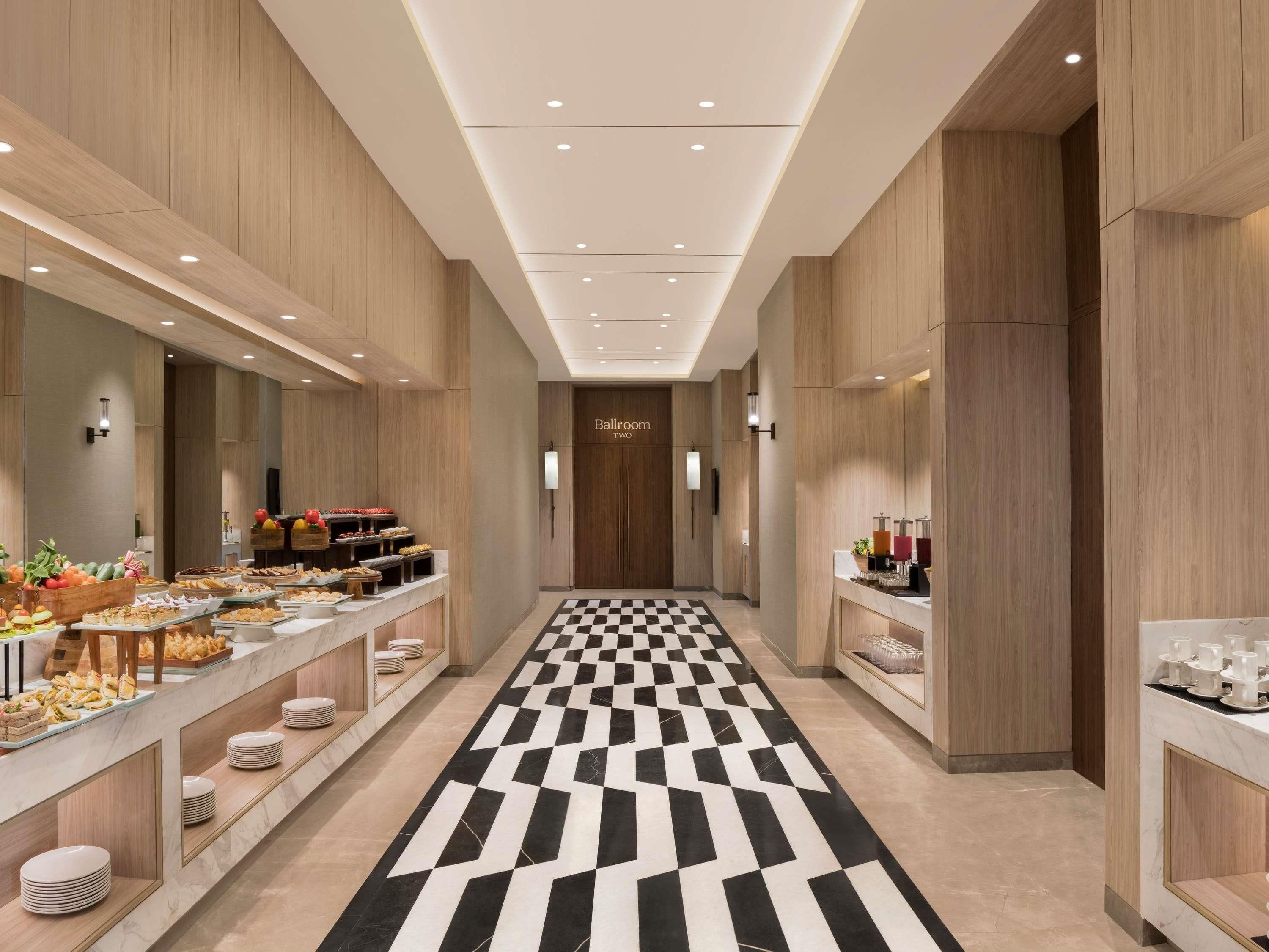 A hotel corridor with a checkered floor, buffet with various food items, and a 'Ballroom' sign.