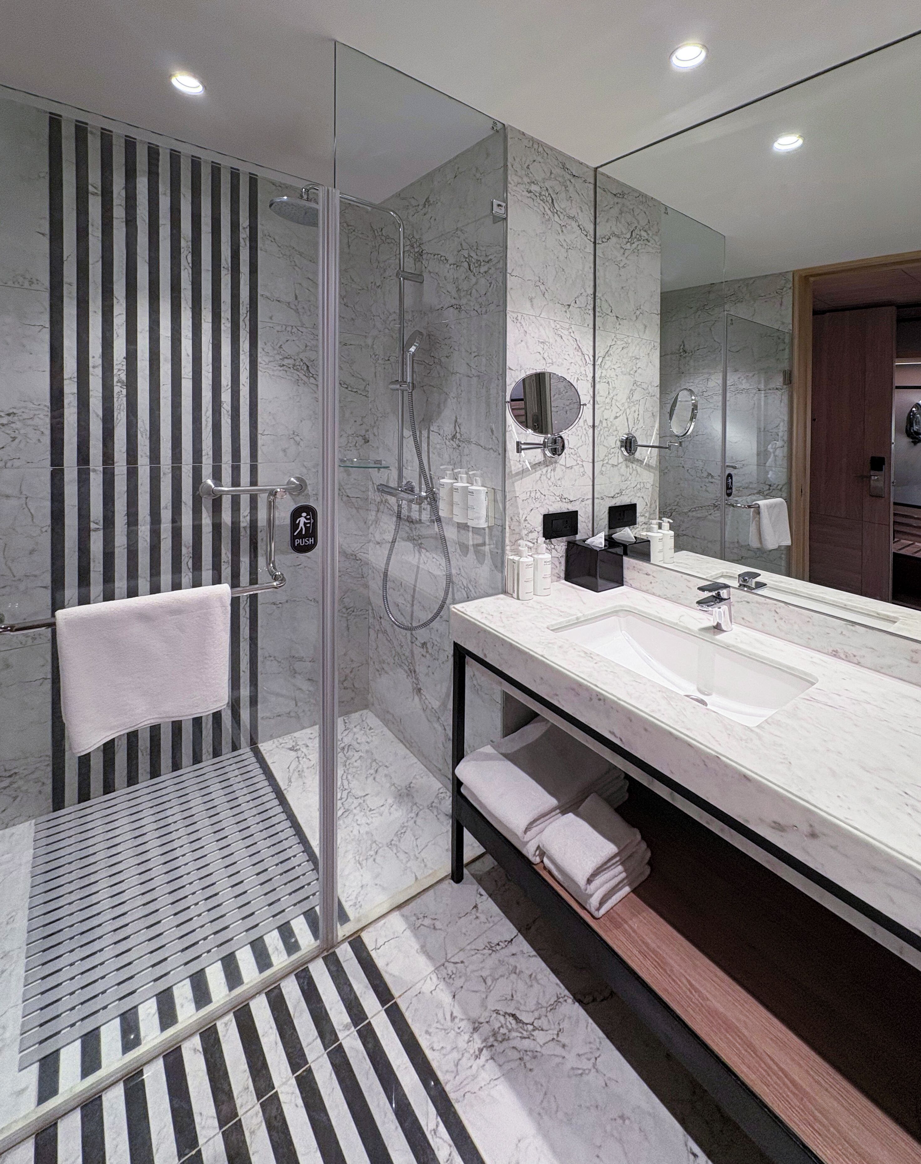 Un baño moderno con ducha de vidrio, un espejo grande y piso de baldosas de mármol.