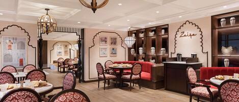 Un restaurante con mesas redondas, sillas estampadas y un sofá rojo central.