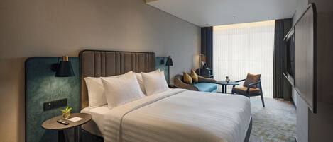 Una camera d'albergo con un letto grande, un comodino con una lampada, una sedia, un tavolino e una televisione.
