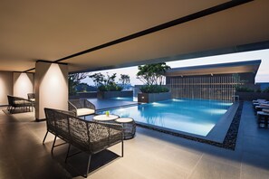 A modern outdoor pool area with lounge chairs and a view of the city skyline. - Mercure Madiun (Madiun)
